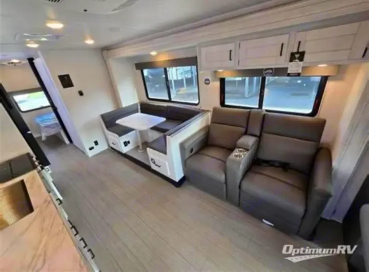 Modern RV rental interior with light floors, a U-shaped dinette, and two plush recliners with cup holders.. East to West Entrada 2025
