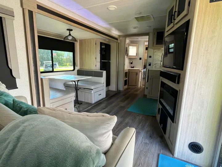 Inviting RV rental interior: living area with sofa, dinette, full kitchen, entertainment center. Features modern light wood accents.. East to West Alta 2022