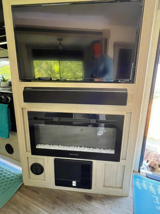 Cozy RV rental amenities: a TV, Furrion soundbar, Greystone fireplace, and a dog peeking in.. East to West Alta 2022