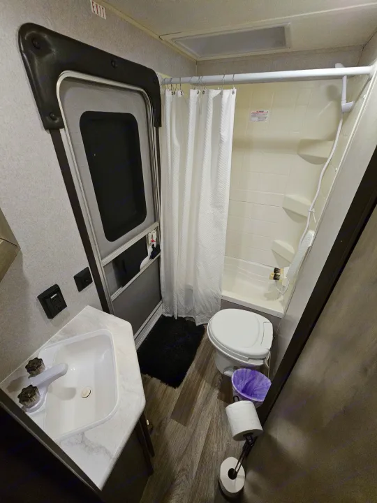 Full bathroom in an RV rental, featuring a corner sink, toilet, shower with curtain, and an exit sign visible above the door.. Forest River Palomino Puma XLE 2019