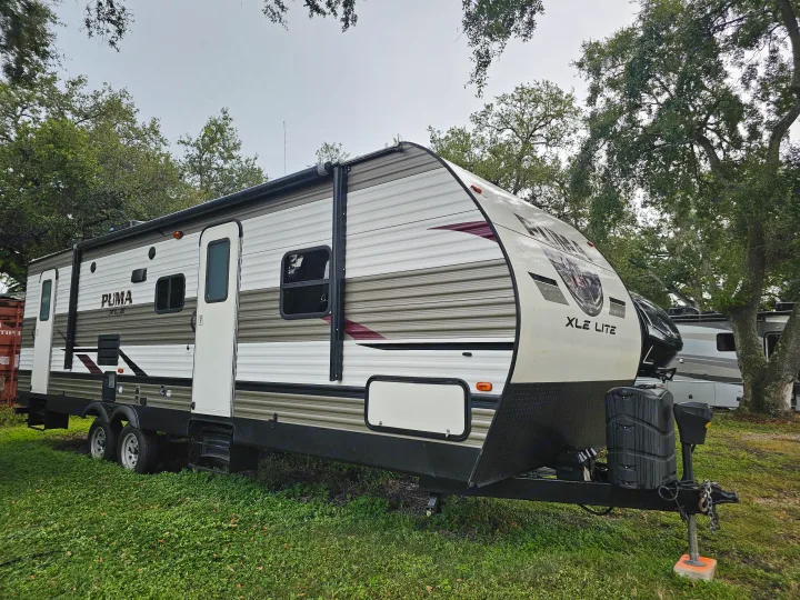 PUMA XLE Lite travel trailer, a white and brown RV rental, parked on green grass under trees for outdoor adventures.. Forest River Palomino Puma XLE 2019
