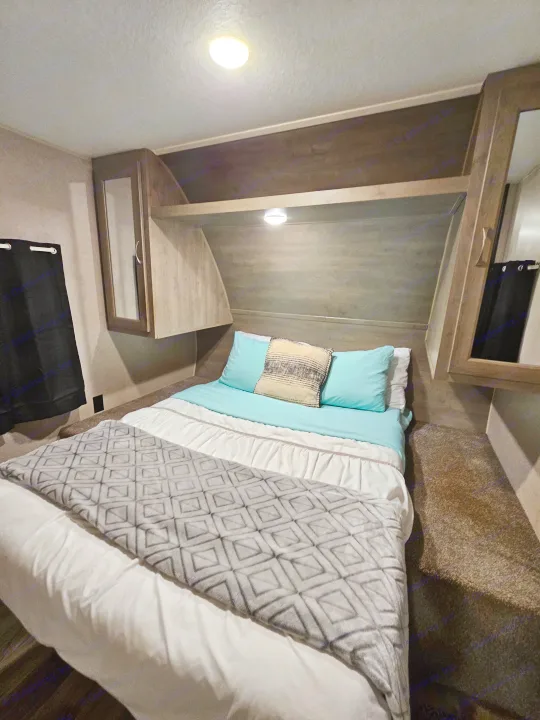 Cozy RV rental bedroom with light blue bedding, overhead cabinets, and soft lighting for your journey.. Forest River Palomino Puma XLE 2019