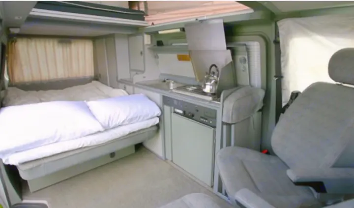 Cozy RV rental interior with bed, kitchenette (stovetop, fridge, sink), and front seat. Perfect for travel.. Volkswagen Multivan 2001
