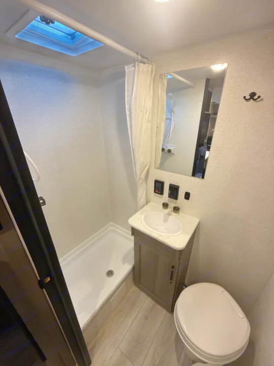 This compact rv rental bathroom features a shower, toilet, vanity with sink, and mirror, all in a bright, modern design.. Keystone RV Hideout Sport 2025