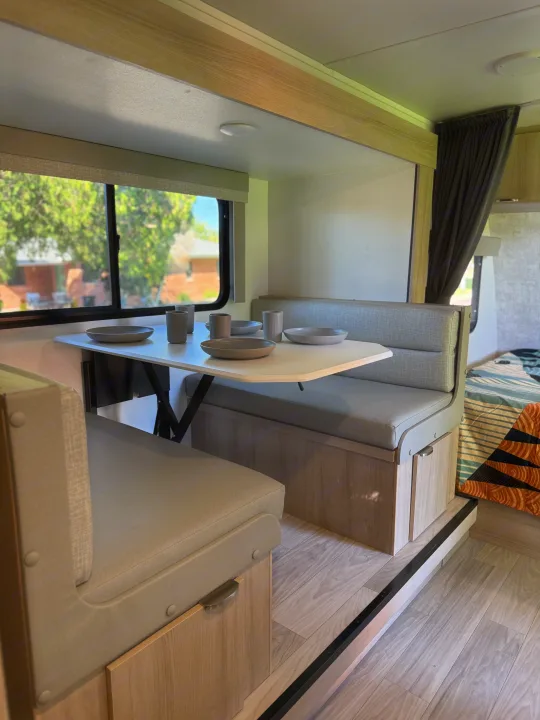 This RV rental interior features a bright dinette with a table set for four, comfy seating, and large windows offering scenic views.. Winnebago Micro Minnie 2100BH 2025