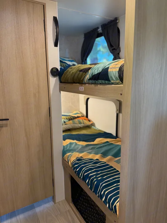 Cozy bunk beds in an RV rental, featuring mountain-themed bedding, window with curtains, and climate control for comfort.. Winnebago Micro Minnie 2100BH 2025