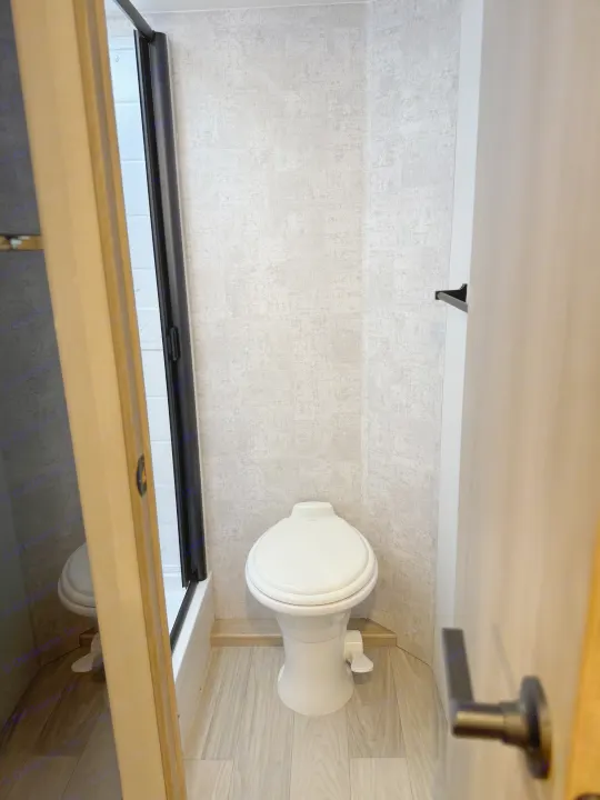 This RV rental features a functional, compact bathroom with a white Dometic toilet, textured gray walls, and a shower stall.. Winnebago Micro Minnie 2100BH 2025