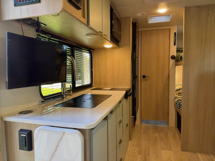 Modern RV rental interior features a kitchen with sink and stovetop, wall-mounted TV, and light wood design. Bright, functional space.. Winnebago Micro Minnie 2100BH 2025