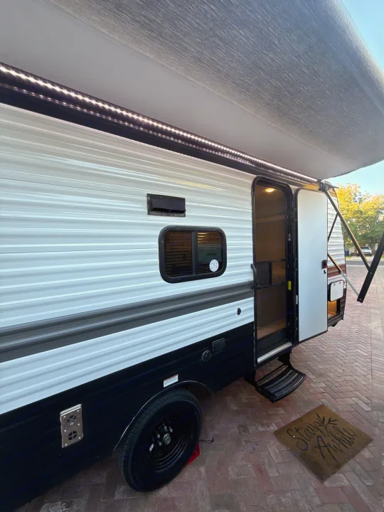 This RV rental is seen from the side, featuring an extended awning with bright LED lights, an open door, and steps, inviting travelers in.. Keystone RV Hideout Sport 2025