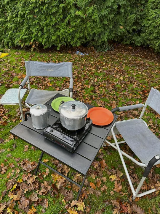 RV rental outdoor cooking setup: portable stove, pot, chairs, and table on a leafy lawn by a hedge. Perfect for camping!. Dodge Caravan 2005