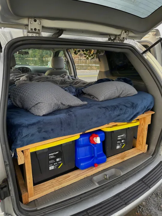 Minivan's cozy bed setup with under-bed storage & water jug, perfect for an RV rental and car camping.. Dodge Caravan 2005