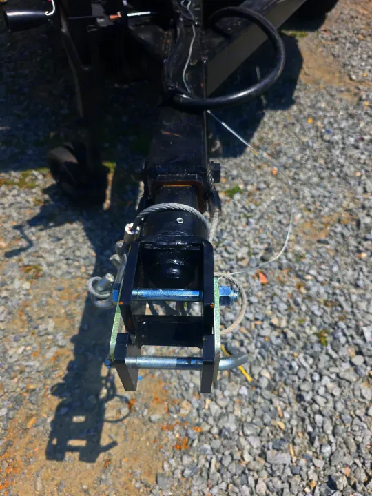 Close-up of an RV rental trailer hitch, showing the black coupler, safety cables, and attachment pins on a gravel surface.. Custom Build Offroad Trailer 2021