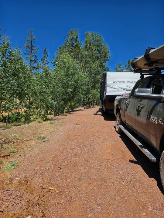 RV rental setup: Truck with a kayak and white travel trailer parked on a gravel campsite among trees under a clear blue sky.. Highland Ridge RV Open Range 2018