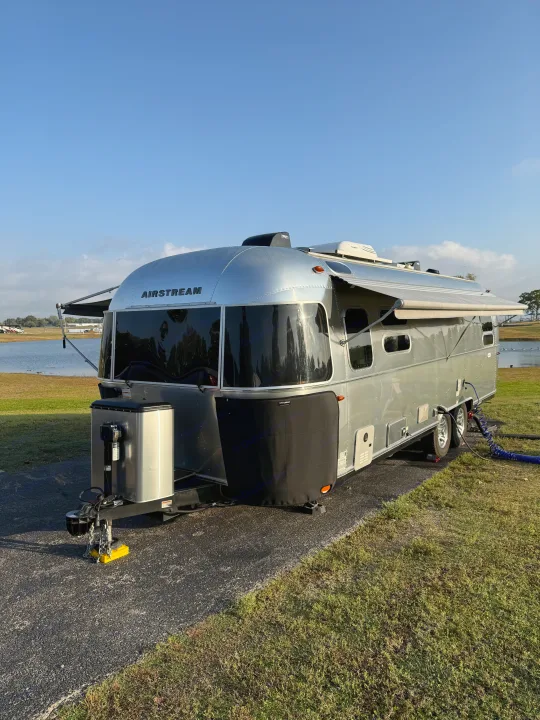 A silver Airstream travel trailer rv rental parked lakeside with awnings out, ready for a serene camping experience.. Airstream Flying Cloud 2022