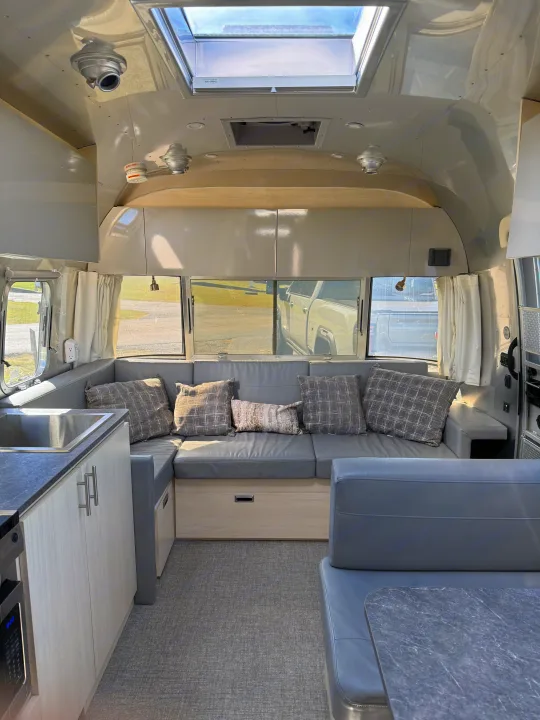 Spacious and modern RV rental interior featuring a gray living area, compact kitchen, and overhead skylight.. Airstream Flying Cloud 2022
