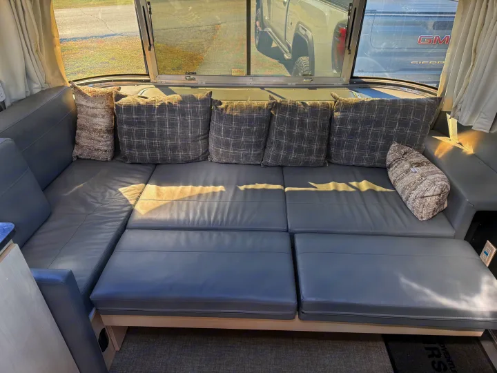 Comfortable gray seating with patterned pillows in a modern rv rental, offering sunny window views of the outdoors.. Airstream Flying Cloud 2022