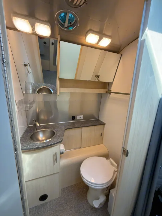 This RV rental bathroom features an efficient design with a sink, mirror, compact toilet, and practical storage for travel.. Airstream Flying Cloud 2022