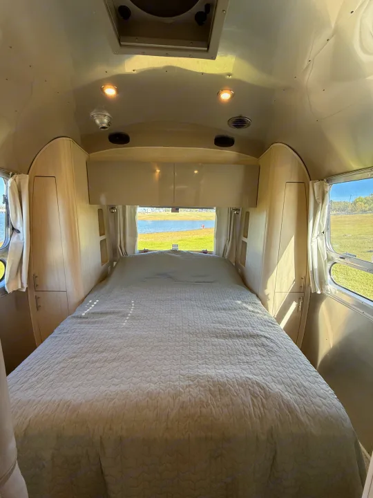 Cozy Airstream RV rental bedroom with a lake view, featuring a plush bed and light wood interior. Ideal for your next adventure!. Airstream Flying Cloud 2022