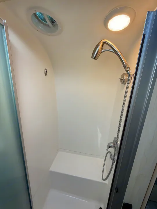 Modern RV rental shower: white interior, flexible handheld showerhead, ceiling vent, built-in seat for comfort.. Airstream Flying Cloud 2022