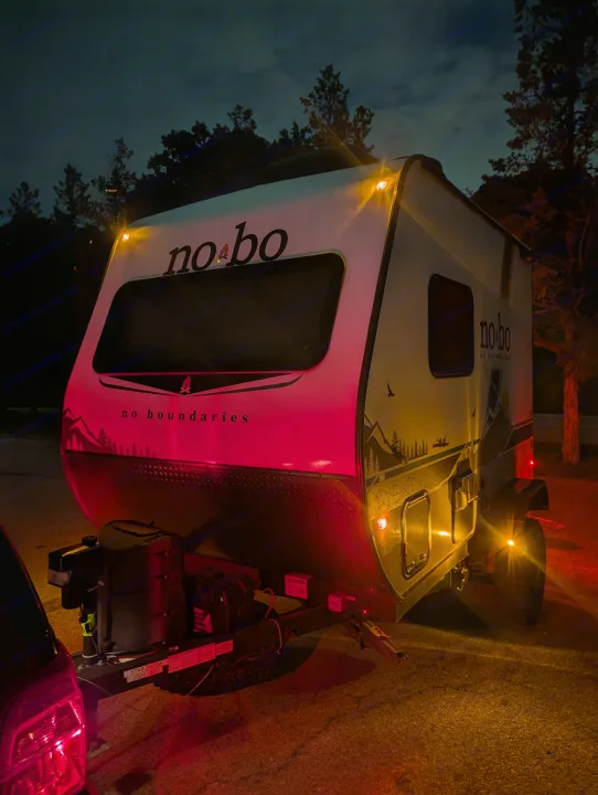Nighttime rv rental featuring a No Boundaries travel trailer hitched to a car, illuminated by vibrant red and amber lights.. No Boundaries 16 2024