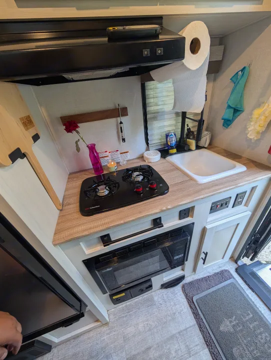 A well-equipped rv rental kitchen showing a two-burner stovetop, sink, microwave, and range hood, perfect for small space living.. No Boundaries 16 2024