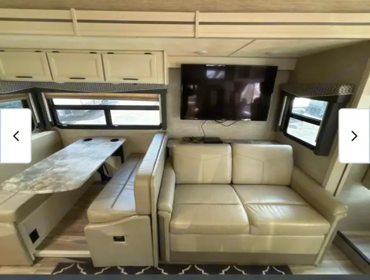 Modern RV rental living space featuring a comfortable dinette, sofa, and mounted TV. Great for your next adventure!. Thor A.C.E. 2021