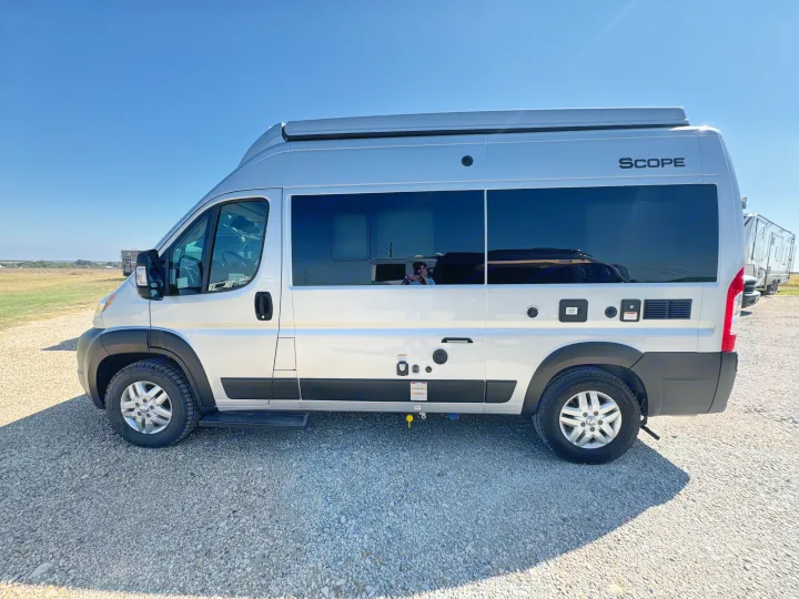 A sleek silver Scope camper van parked on gravel under a clear sky. Perfect for an RV rental getaway.. Dodge Ram 1500 2022