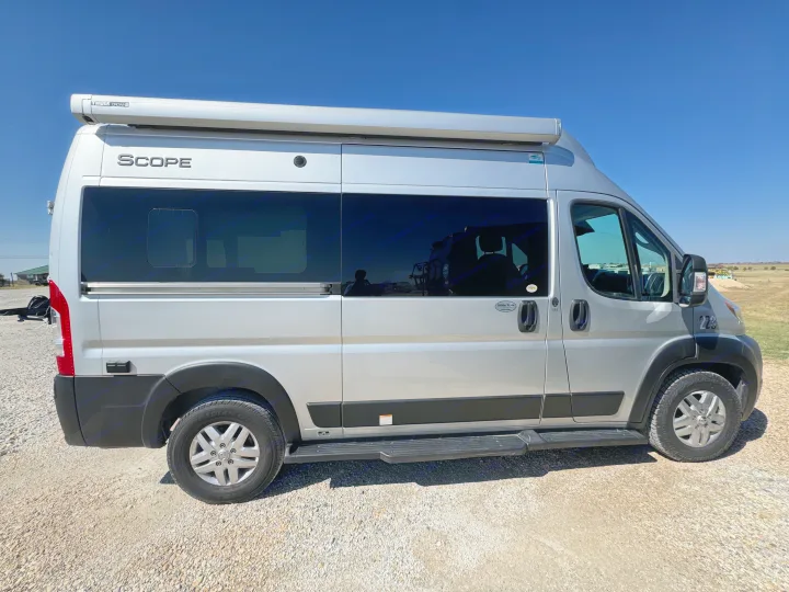 Silver Scope camper van rv rental with awning & tinted windows, parked on gravel under a clear blue sky, ready for travel.. Dodge Ram 1500 2022
