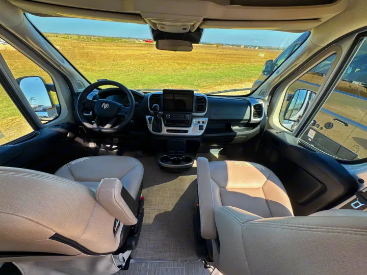 Inside an RV rental, the spacious driver's area has beige seats, a modern dashboard, and clear views of the open field.. Dodge Ram 1500 2022