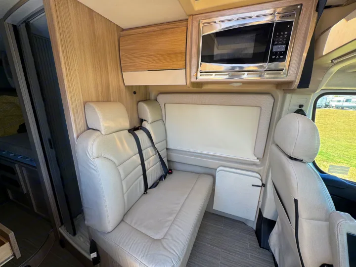 RV rental interior featuring comfortable passenger seating with seatbelts, a microwave, and a fold-down table for travel.. Dodge Ram 1500 2022