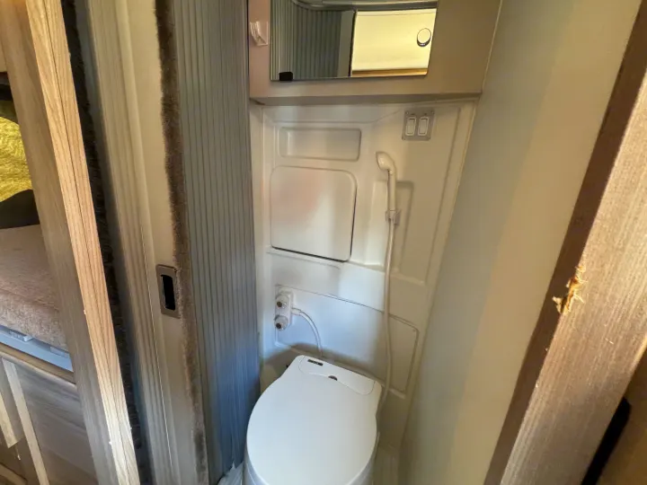 Compact RV rental bathroom featuring a white toilet, wall-mounted shower head, and small mirror above.. Dodge Ram 1500 2022