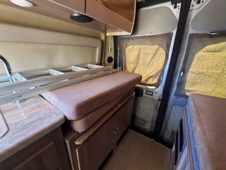 Interior of an RV rental showing a compact kitchenette with sink, cushioned seating, cabinetry, and window shades.. Dodge Ram 1500 2022