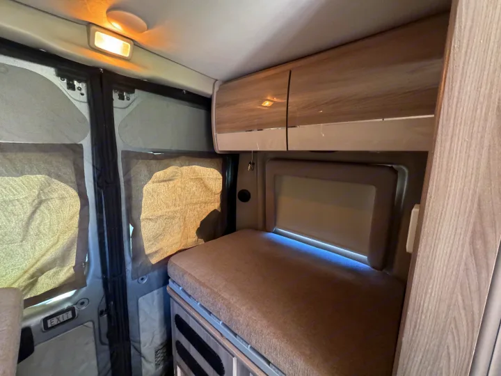 Modern rv rental interior featuring a cushioned bed, sleek overhead storage, and screened windows for comfortable journeys.. Dodge Ram 1500 2022