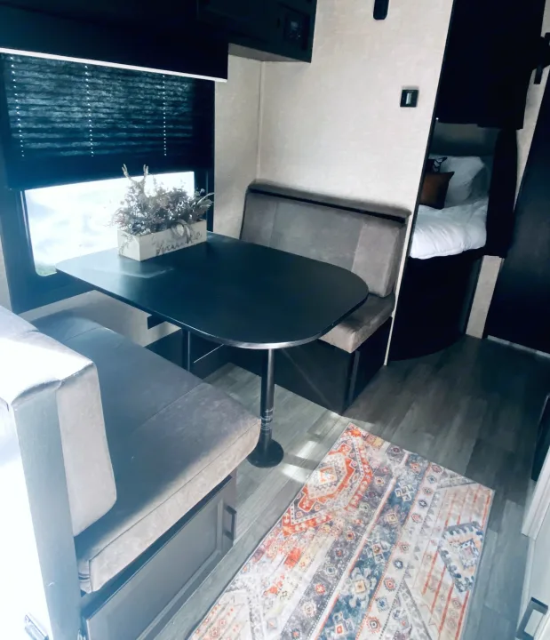 Modern RV rental interior: comfortable dinette, window with blind, colorful rug, and a peek at the sleeping area.. Jayco Jay Flight 2023