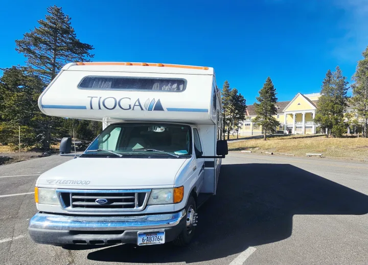 White Tioga rv rental parked under a bright blue sky, with pine trees and a grand yellow lodge in the background.. Tioga SL 2006