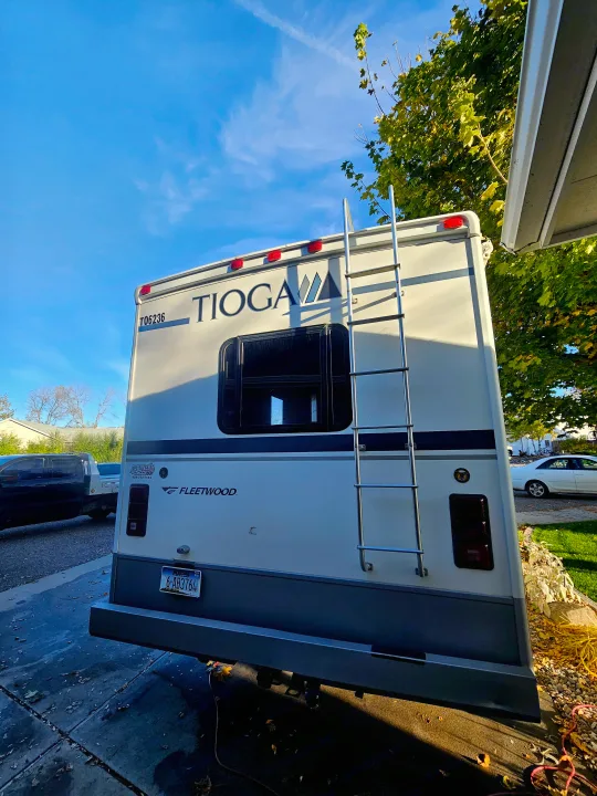 Experience the open road! This white Tioga Fleetwood RV, ready for your next rv rental trip, features a rear ladder against a bright blue sky.. Tioga SL 2006