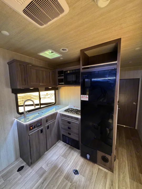 RV rental interior: A modern kitchen with wood cabinets, a sink, stove, microwave, refrigerator, and LED-lit countertops.. Genesis Supreme Rv Ragen 2025