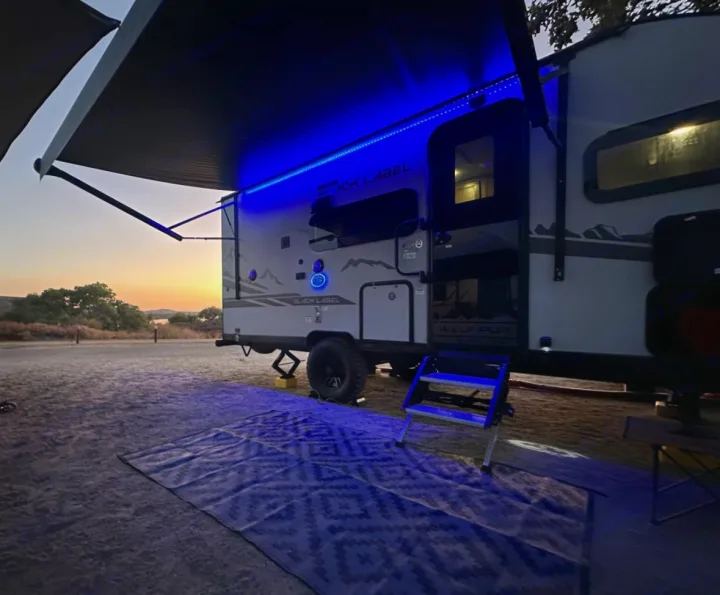 RV rental camping at sunset, featuring vibrant blue awning lights and an outdoor mat for evening relaxation.. Forest River Cherokee Wolf Pup 2023