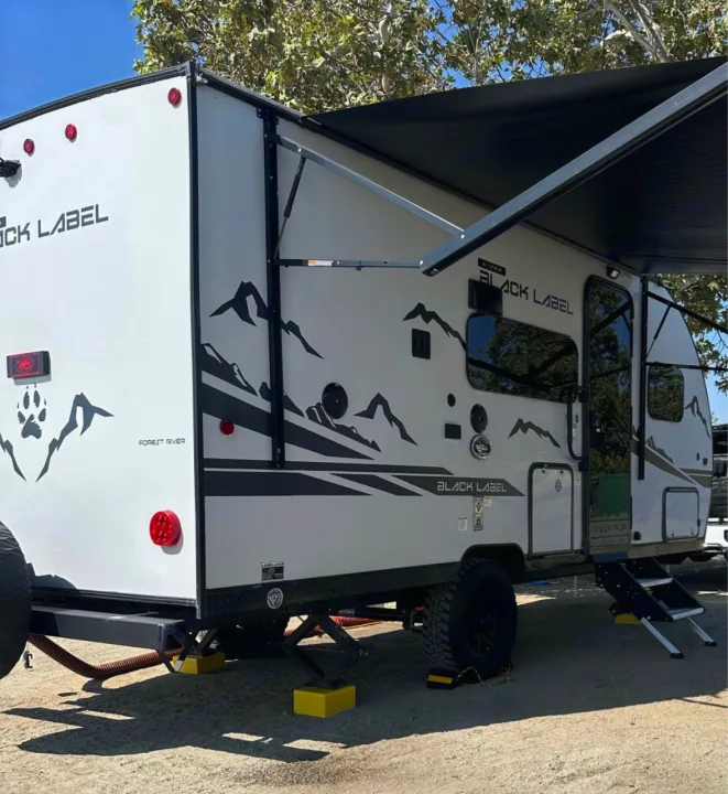 White 'Black Label' rv rental with mountain graphics, awning extended, set up for outdoor camping. Ready for adventure.. Forest River Cherokee Wolf Pup 2023