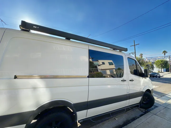 White Mercedes-Benz Sprinter RV rental van, with roof awning & side steps, parked on a sunny street. Ready for adventure.. Mercedes-Benz Sprinter 2014