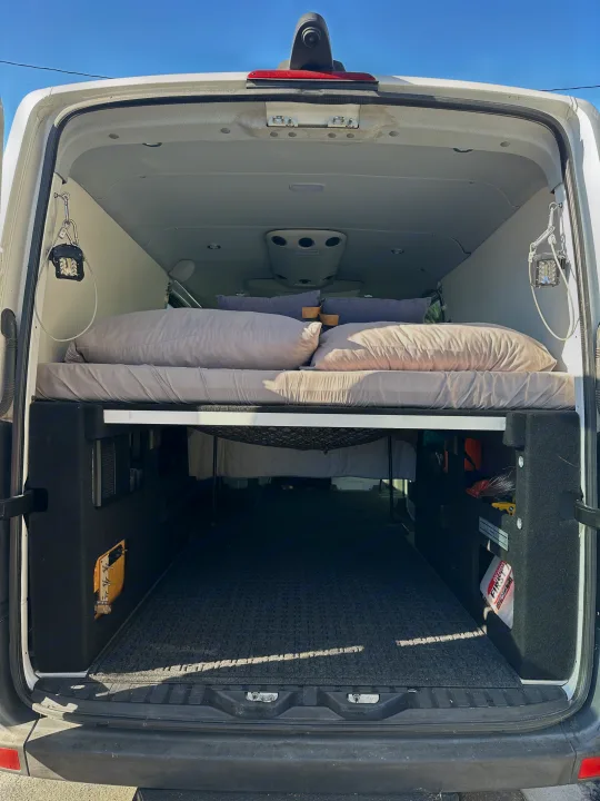 RV rental camper van interior. Elevated bed platform with pillows, spacious under-bed storage, and utility lights.. Mercedes-Benz Sprinter 2014