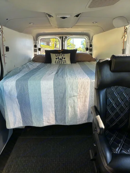 RV rental: Cozy camper van interior featuring a comfortable bed with a "Happy Camper" pillow and a black leather seat.. Mercedes-Benz Sprinter 2014
