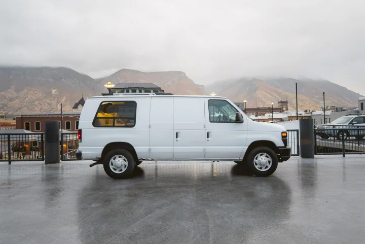 A white van, possibly an RV rental, sits on wet pavement with cloudy mountains and the iconic Provo "Y" in the distance.. Ford Econoline E250supercab 2008