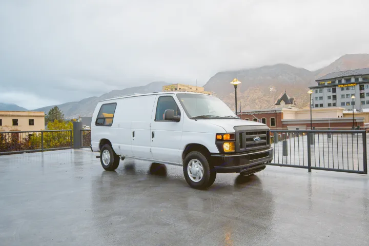 White Ford cargo van, ideal for RV rental conversion, parked on a wet deck overlooking city buildings and mountains.. Ford Econoline E250supercab 2008