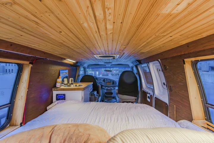 Cozy rv rental camper van interior with wood paneling, bed, small kitchen, and front cab view. Ideal for van life adventures.. Ford Econoline E250supercab 2008