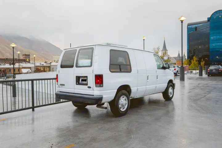 Explore with an rv rental! White van parked on wet street with city buildings, cloudy mountains, and streetlights.. Ford Econoline E250supercab 2008