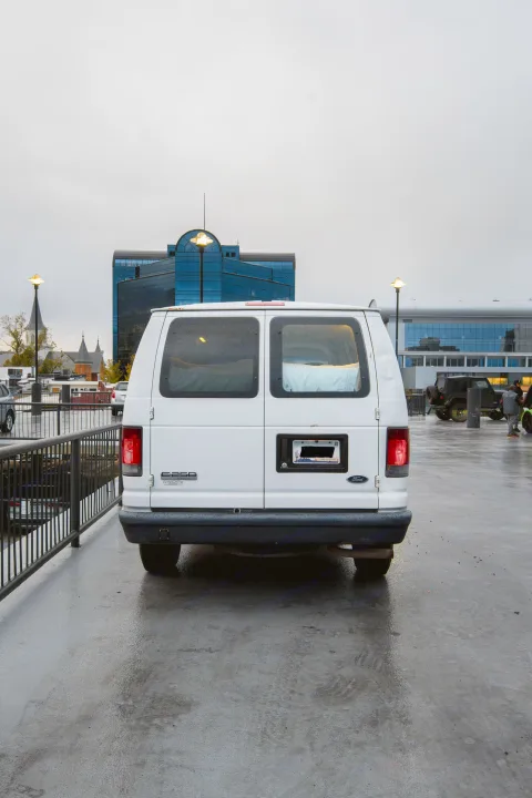 Rear of a white Ford E-350 van (an RV rental) on a wet urban street with diverse architecture under an overcast sky.. Ford Econoline E250supercab 2008