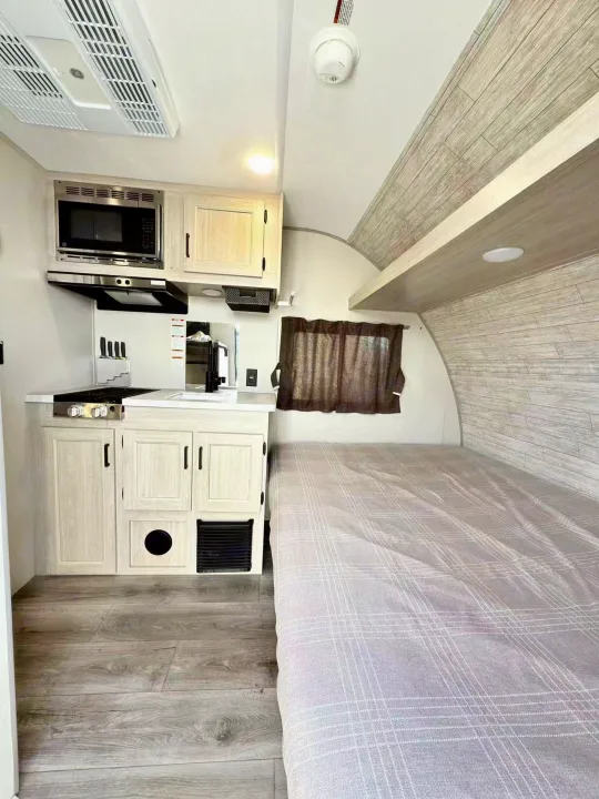RV rental: Bright, modern interior with a compact kitchenette (microwave, stove, sink), light wood cabinets, and a comfortable bed.. Coachmen Catalina Summit 7 134BHX 2025