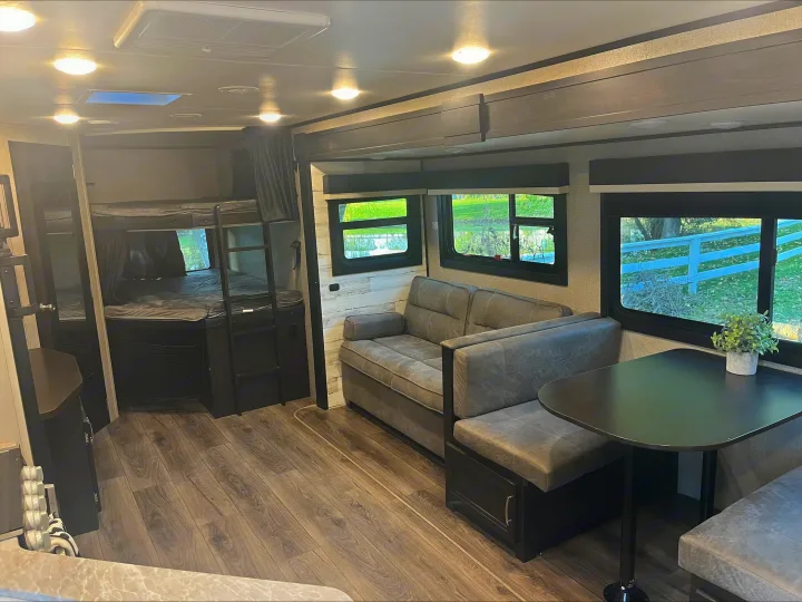 RV rental: Inside view of a modern RV with bunk beds, a gray sofa, and a dinette next to large windows.. Jayco Jay Feather 2021