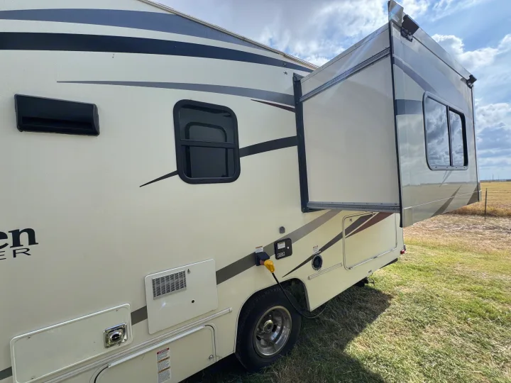 Side view of an RV rental with an extended slide-out, showcasing windows, power hookup, and vents, parked on grass.. Forest River Coachmen Freelander 2019